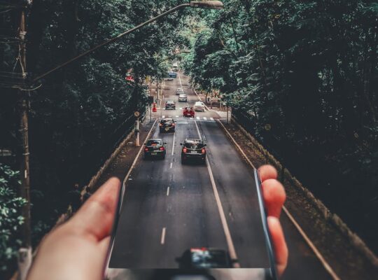 forced perspective photography of cars running on road below smartphone