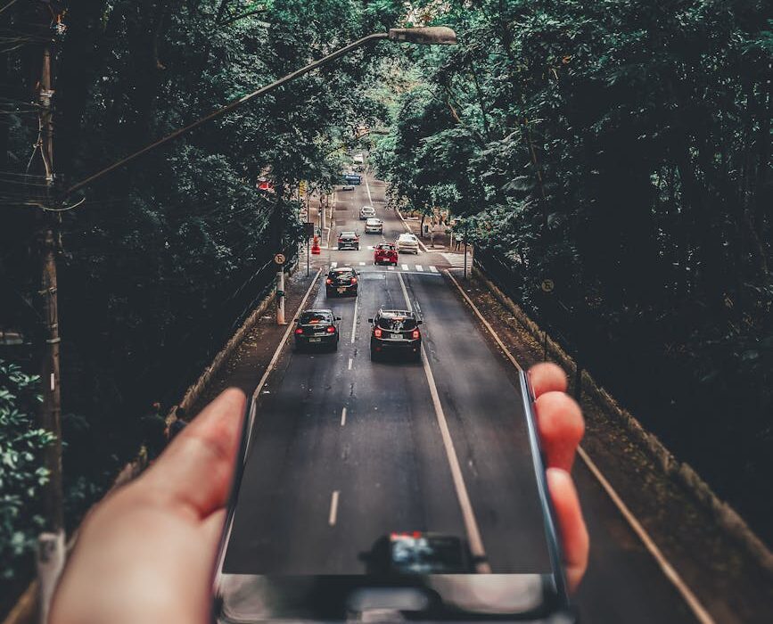 forced perspective photography of cars running on road below smartphone